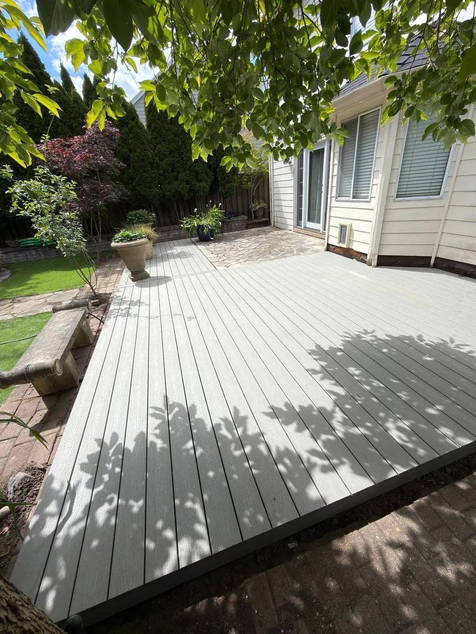 New gray composite deck built over a paver patio in a backyard