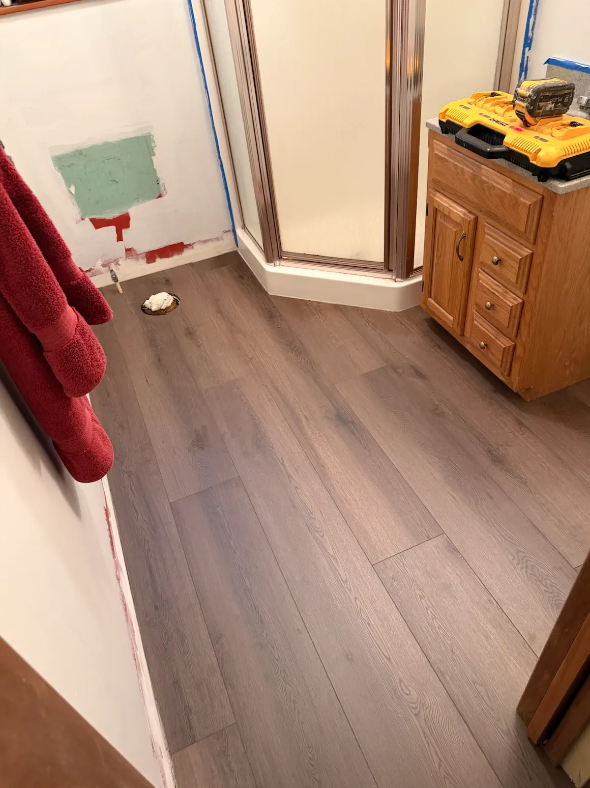 Vinyl plank in a bathroom, fitted around a corner shower base and an oak vanity