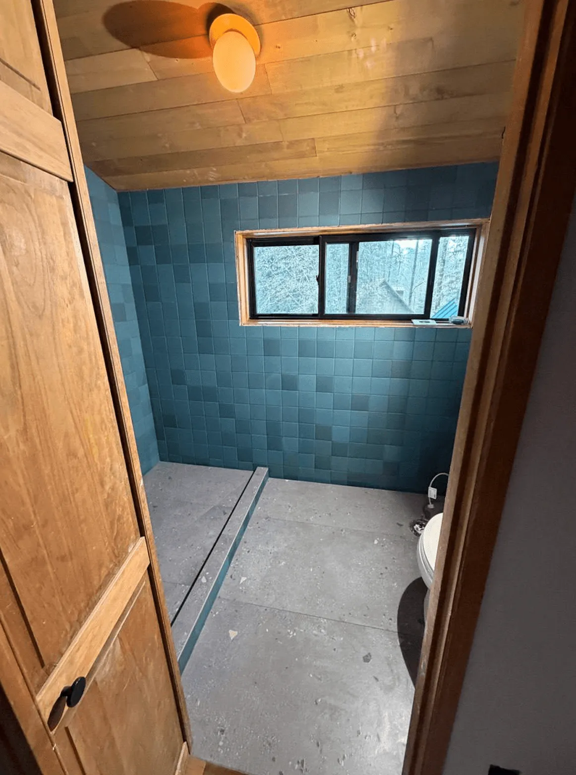 Bathroom with blue-green square wall tile, large terrazzo-look floor tile and a wood plank ceiling