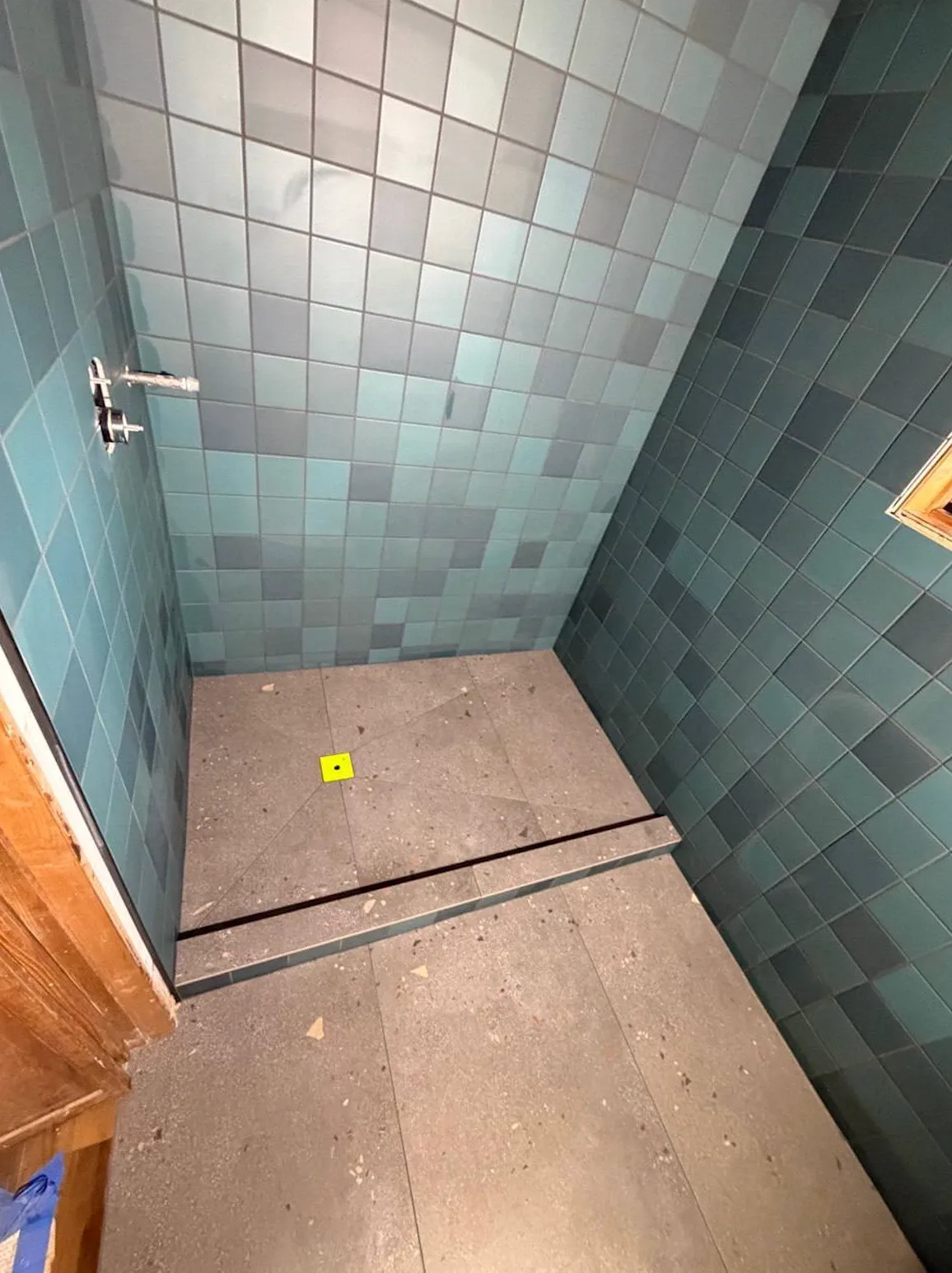 Walk-in shower with mixed blue-green square wall tile and a terrazzo-look floor sloped to the drain behind a low curb
